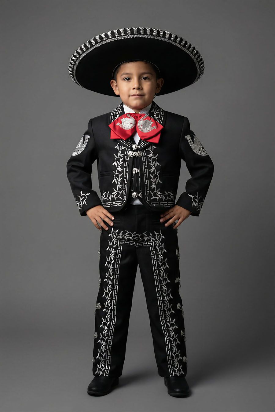 Boy wearing a black and silver charro mariachi suit with silver embroidered horseshoes and horse heads, silver metal buttons, matching sombrero, vest, white shirt, and bow tie.
